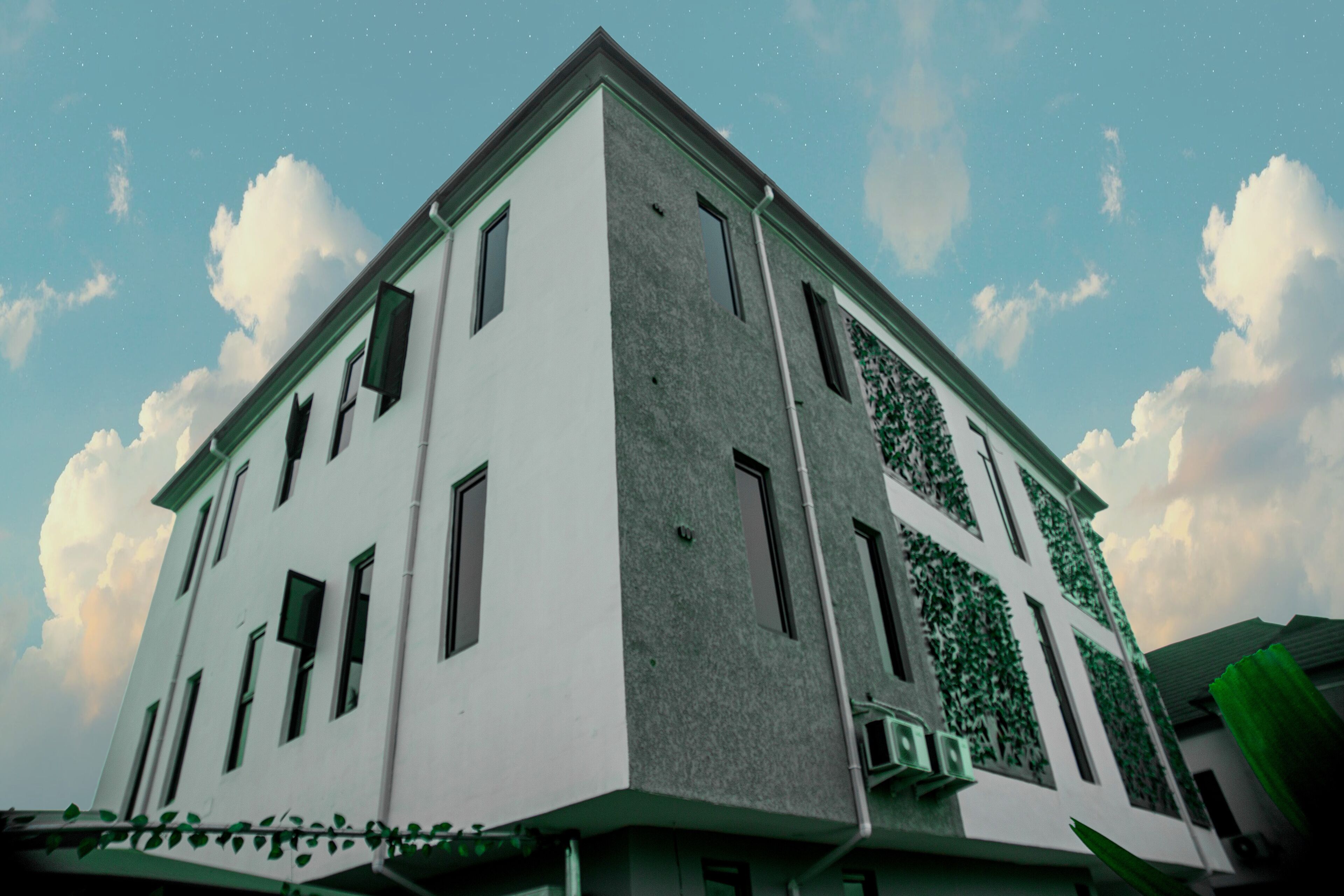 Un bâtiment moderne à la façade blanche et aux touches de vert, doté de nombreuses fenêtres et d’un toit plat.