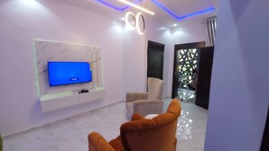 A modern living room with a flat-screen TV mounted on a marble wall, a beige sofa, and a glass coffee table. - RichVilla Apartments & Hotels (Lagos)