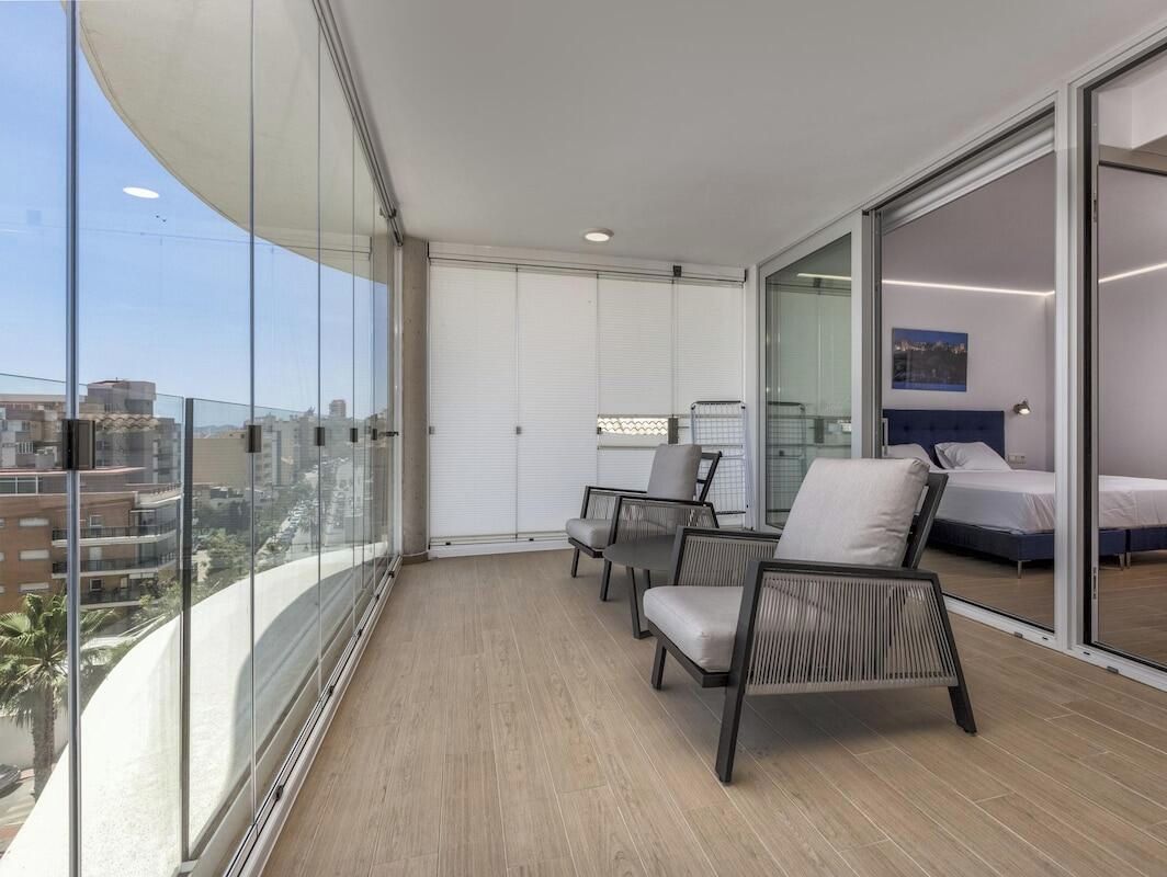 A balcony with a view of the city, a bed, and a seating area with chairs.
