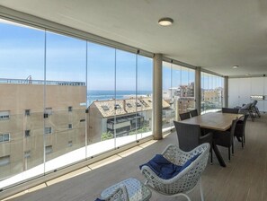 A spacious balcony with large windows overlooking a cityscape and the sea.