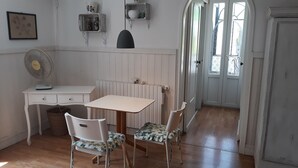 Quarto com escrivaninha branca, duas cadeiras com estofamento floral, radiador e porta que dá para o exterior.