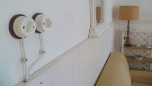 Quarto com parede branca, janela com espelho e luminária sobre uma mesa de madeira.