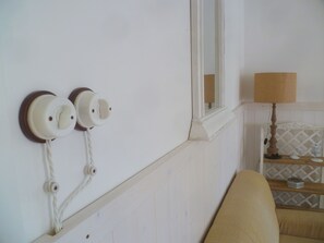Ein Zimmer mit weißer Wand, einem Fenster mit Spiegel und einer Lampe auf einem Holztisch.