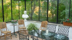 Um solário com mesa de vidro, cadeiras de vime e uma escultura de busto.