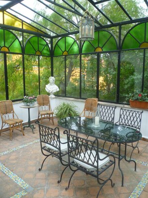 Ein Wintergarten mit Glastisch, Korbstühlen und einer Büstenstatue.