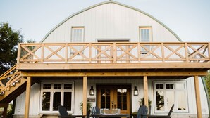 Een grote witte schuur met een houten terras en een buiten zitgedeelte.