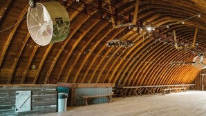 Een zolderkamer met een hoog houten plafond, een grote ventilator en lichtslingers.