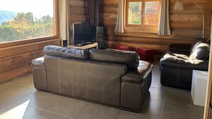 A log cabin interior with a leather sofa, a television, and a window with curtains. - Chalet L'estaca: Vue sur la Nature (Font-Romeu-Odeillo-Via)