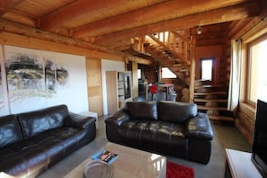 A spacious living room with a large black leather sofa, a glass coffee table, and a red rug. A staircase leads to an upper level.