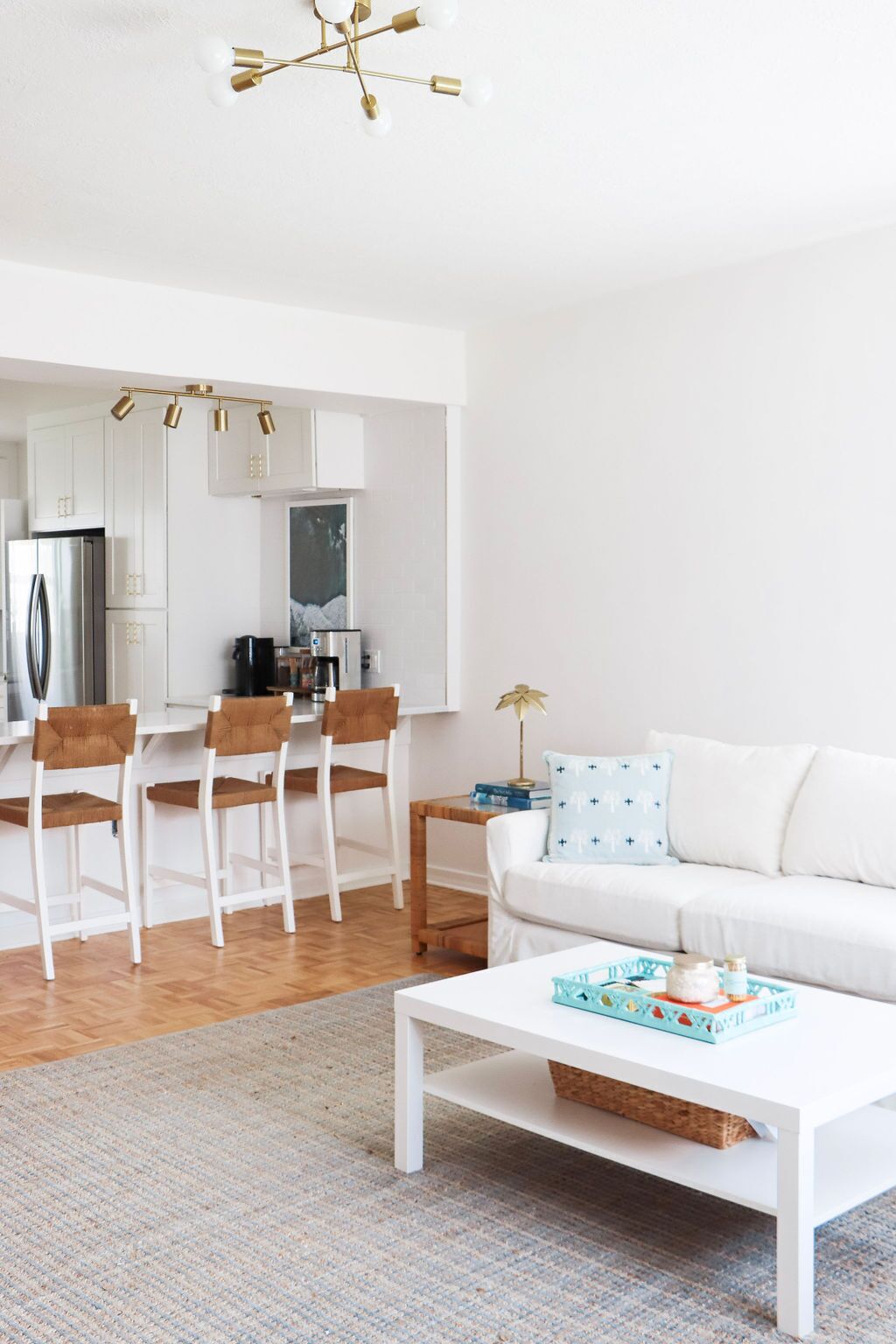 Een moderne woonkamer met een witte bank, een bijzettafeltje en een eethoek met stoelen, met een keuken op de achtergrond.