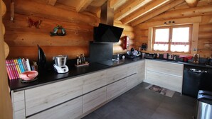A modern kitchen with wooden walls, a black countertop, and a window with curtains. - Chalet les Petits Loups (Font-Romeu-Odeillo-Via)