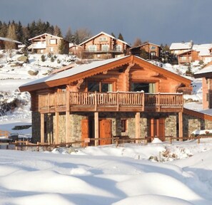 A wooden chalet with a balcony, surrounded by snow-covered hills.