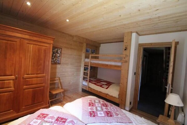 A wooden cabin bedroom with bunk beds, a wardrobe, and a small desk.