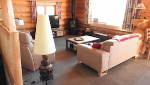 A cozy log cabin interior with a sofa, a table, a lamp, a television, and a wood-burning stove. - Chalet les Petits Loups (Font-Romeu-Odeillo-Via)