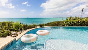 A clear blue pool with two inflatable rings, surrounded by lush greenery and a view of the ocean.