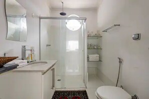 A bathroom with a glass-enclosed shower, a toilet, a sink with toiletries, and a mirror. - Casa Inteira (São Paulo)