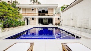 Ett modernt hus i två våningar med en swimmingpool, en uteplats och en trädgård.
