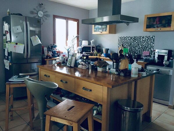 A kitchen with a wooden island, stainless steel appliances, and a window. - Chambre Dans Maison Face à la Rivière Dain (Varambon)