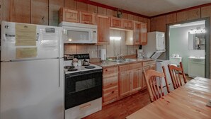 Une cuisine avec des meubles de rangement en bois, une cuisinière, un four à micro-ondes, un réfrigérateur et une table à manger avec des chaises.
