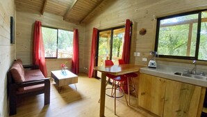 A wooden cabin interior with a dining area, kitchen, and seating space. - Cabinas Costa Tropicana (Bahía Ballena)