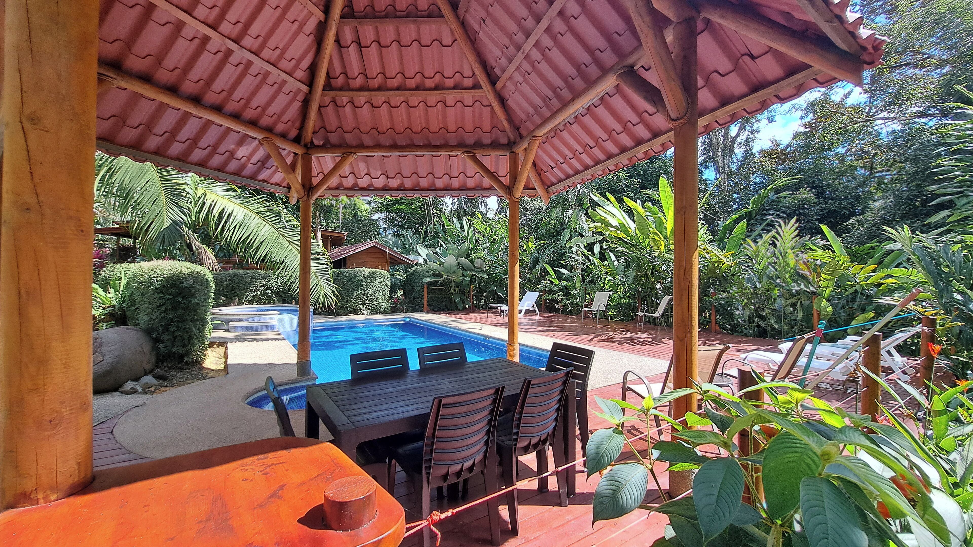 A covered outdoor area with a pool, wooden deck, and seating.