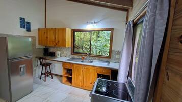 A compact kitchen with wooden cabinets, a refrigerator, a stove, and a window providing a view of greenery.