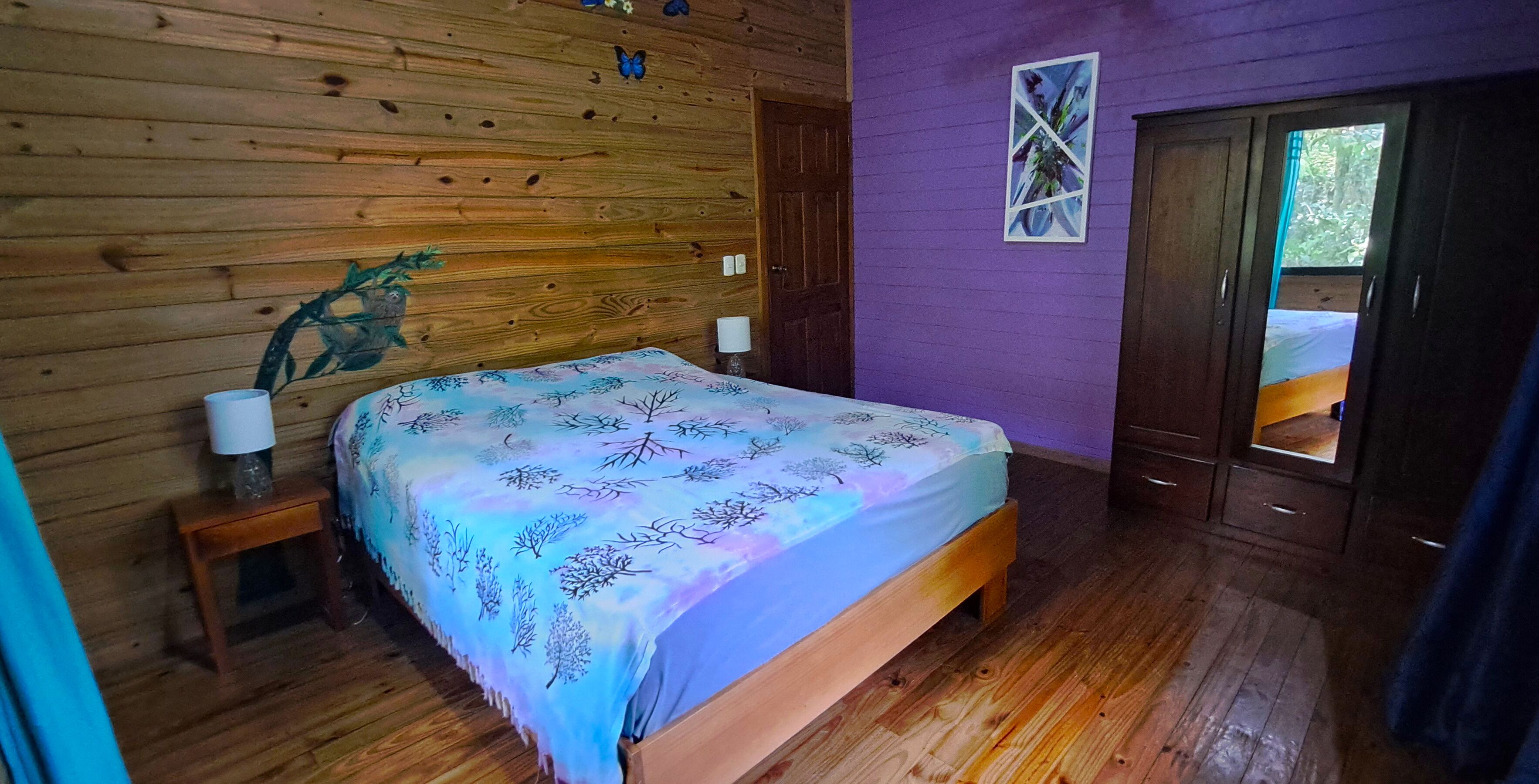 A wooden cabin bedroom with a bed, a nightstand, a wall-mounted lamp, and a door leading outside.