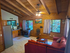 A cozy cabin interior with a kitchenette, a dining area, a sofa, and a ceiling fan. - Cabinas Costa Tropicana (Bahía Ballena)