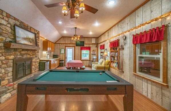 A pool table in a room with wooden walls, a fireplace, and a cozy seating area.
