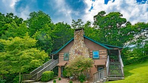 A rustic cabin with a stone chimney, wooden exterior, and a staircase leading to the entrance.