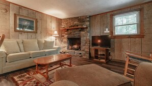 A cozy living room with a stone fireplace, a television on a wooden stand, a sofa, and a coffee table.