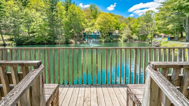 Terraza de madera con vista a un lago y casas al fondo.