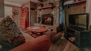 A cozy living room with a stone fireplace, a television, and a patterned throw blanket on a couch.