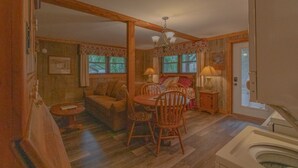 A cozy room with a wooden dining table, chairs, a sofa, and a small side table with a lamp.