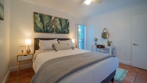 A neatly arranged bedroom with a large bed, a bedside table with a lamp, a small desk with a chair, a globe, and a mirror on the wall. - Comfy 1b getaway w/ BEACH ACCESS & full amenities (Key Biscayne)