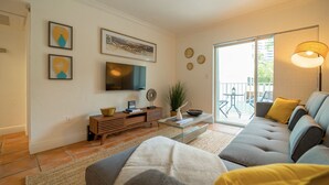 A modern living room with a sofa, a coffee table, a TV, and a balcony with outdoor seating. - Comfy 1b getaway w/ BEACH ACCESS & full amenities (Key Biscayne)