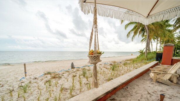 A beach view with a macrame hanging planter, a concrete barrier, and beach chairs. - Comfy 1b getaway w/ BEACH ACCESS & full amenities (Key Biscayne)