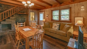 A cozy cabin interior with a wooden dining table, chairs, a sofa, a fireplace, and a staircase. - Cozy Lakeside Cabin #15 - Sleeps 6 - Full kitchen + fireplace - between Boone & Blowing Rock NC (Blowing Rock)