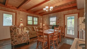 A cozy cabin interior with a wooden dining table, chairs, a floral armchair, a sofa, and a kitchen area with a refrigerator and sink. - Cozy Lakeside Cabin #15 - Sleeps 6 - Full kitchen + fireplace - between Boone & Blowing Rock NC (Blowing Rock)