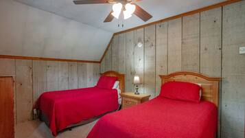 Una camera da letto con due letti singoli, poggiagambe in legno, una ventola a soffitto e un comodino con una lampada.
