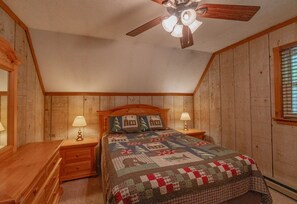 Ein gemütliches Schlafzimmer mit Holzwänden, einem hölzernen Bettgestell, einer Bettdecke, zwei Nachttischen mit Lampen und einem Deckenventilator.