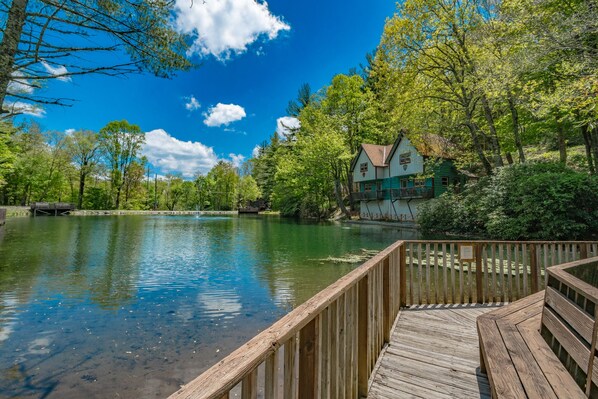Una terraza de madera con vistas a un lago tranquilo y una casa al fondo.