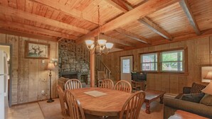 Un intérieur en bois avec une table de salle à manger ronde, des chaises en bois, un mur en pierre, un escalier et un téléviseur.