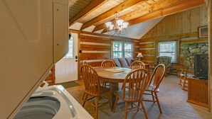 Interior acogedor de una cabaña de madera con comedor, chimenea de piedra y un amplio ventanal.