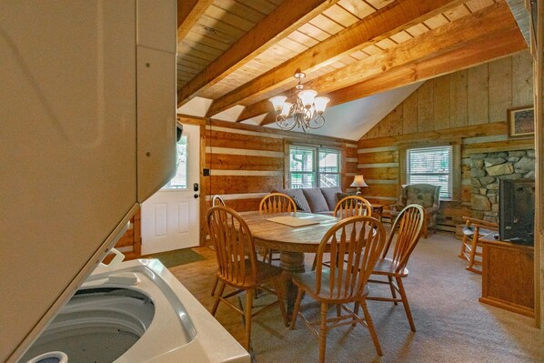 Interior acogedor de una cabaña de madera con comedor, chimenea de piedra y un amplio ventanal.