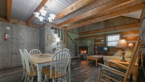 A rustic interior with a dining table, chairs, a fireplace, a sofa, and a rocking chair.