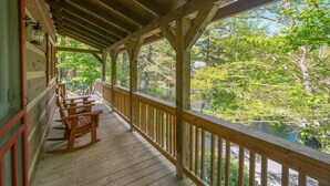 A wooden porch with rocking chairs and a view of a forested area.