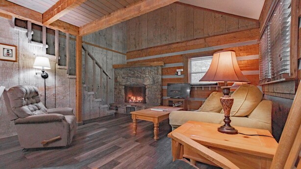 A cozy cabin interior with a stone fireplace, wooden furniture, and a comfortable seating area.