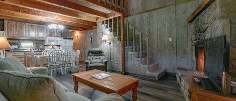 Un interior rústico con una zona de comedor de madera, una chimenea y una escalera que sube a un nivel superior.