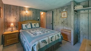 Ein Schlafzimmer mit Holzwand, einem Bett mit gemustertem Überwurf, einem Nachttisch mit Lampe, einer Kommode und einem Kleiderschrank.